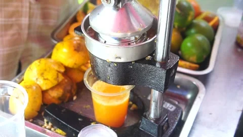 A person uses a machine to prepare a drink, incorporating fresh orange fruit int Video stock 301582539