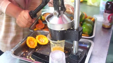 A person uses a machine to prepare a drink, incorporating fresh orange fruit int Video stock 301582545