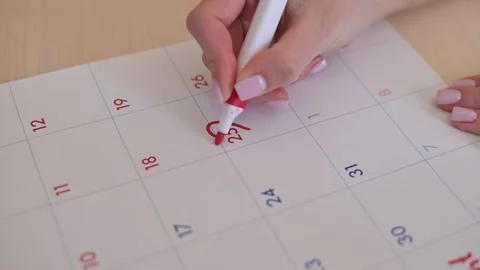 A person uses a marker to write dates on a calendar. The calendar features 스톡 동영상 337556571