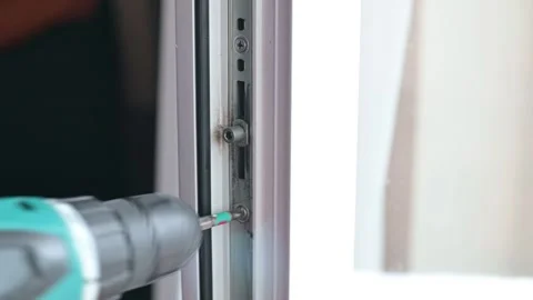 A person uses a power drill to install screws into a window frame, focusing on 스톡 동영상 337111532