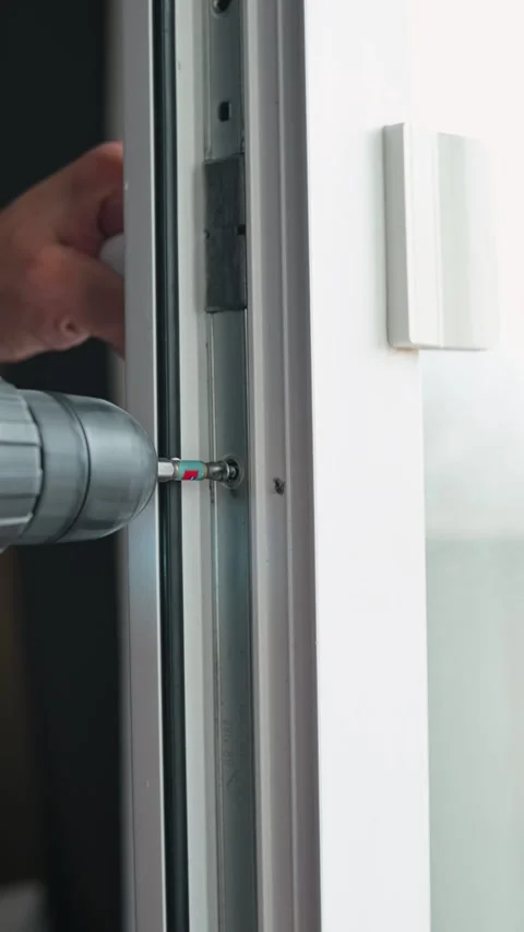 A person uses a power drill screwdriver to secure screws into a window frame. 스톡 동영상 337112612