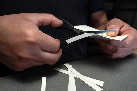 A person uses scissors to cut thin strips of paper. The hands hold the scis.. Stock Photos
