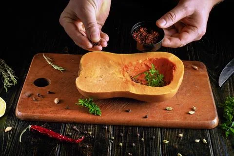 A person uses a small container to add spices to a hollowed butternut squash  Stock Photos