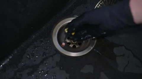A person uses a specialized tool to clear debris from a kitchen sink drain. This Vidéo 337642825