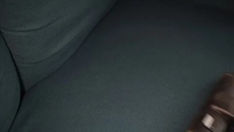 A person uses a vacuum cleaner to clean a couch in a living room. The action Video stock 339005151
