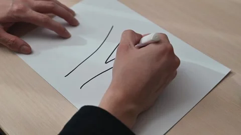 A person uses a white marker to draw lines on a blank sheet of paper on a wooden Stockbeeldmateriaal 337549876