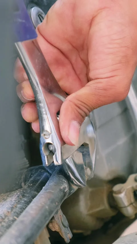 A person using an adjustable wrench to tighten a bolt on a motorcycle Vidéo 332997874