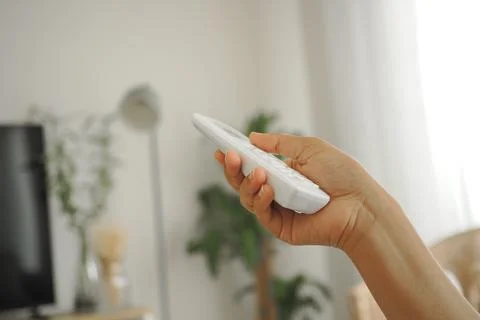 A person is using a air condition remote control while sitting in a living room Stock Photos