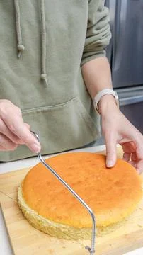 Person using a cake leveler to slice a freshly baked round sponge cake on a Stock Photos