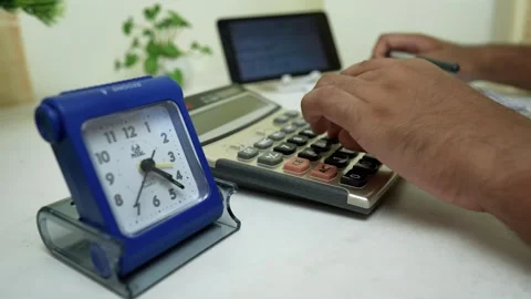 Person using a calculator with a clock on the desk Stock Footage 320726690