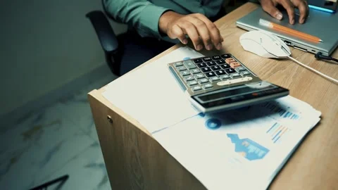 Person using a calculator at a desk with documents and a laptop Stock Footage 315981843