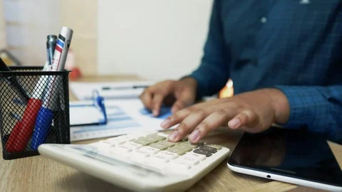Person using a calculator at a desk with documents and pens Stock Footage 318056829