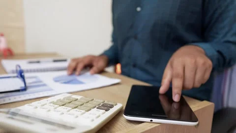 Person using a calculator at a desk with documents and pens Stock Footage 318056843