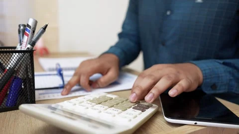 Person using a calculator at a desk with documents and pens Stock Footage 318056865