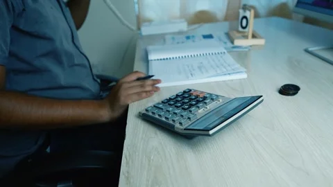 Person using a calculator at a desk with a notebook and computer Stock Footage 315982869