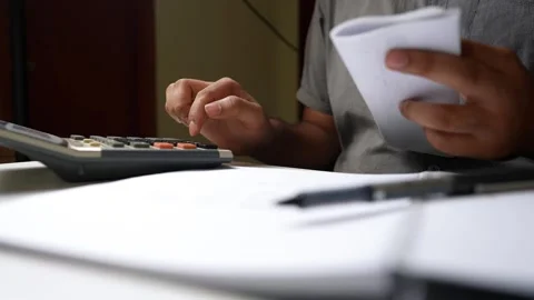 Person using a calculator with a notepad and pen on a desk shot Stock Footage 318056704