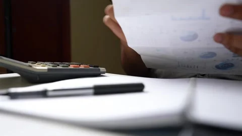 Person using a calculator with a notepad and pen on a desk shot Stock Footage 318056709