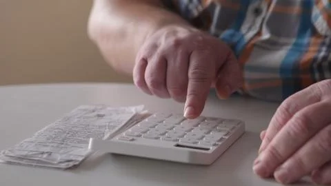Person using a calculator while looking at a receipt in a bright room during the Stock Photos
