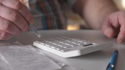 Person using a calculator while reviewing receipts at a table in a bright Stock Photos