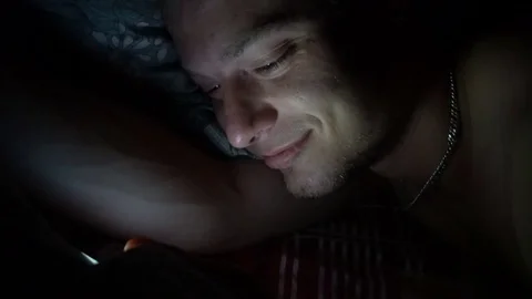Person using cellphone in bed. Smiling Man using smartphone mobile cellphone in Stock Footage 78809677