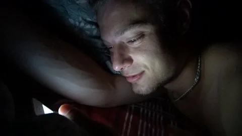 Person using cellphone in bed. Smiling Man using smartphone mobile cellphone in Stock Footage 78810076