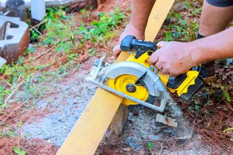 Person using circular saw to cut wooden plank in construction area Stock Photos