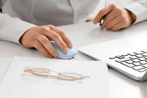 Person using computer mouse next to laptop and glasses Stock Photos