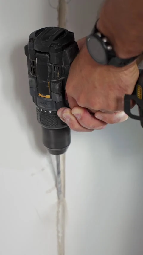 Person using cordless power drill on plaster wall during DIY work Stock Footage 345600941