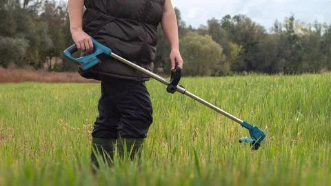 Person using electric grass trimmer on green lawn in countryside field. Conce Stock Photos