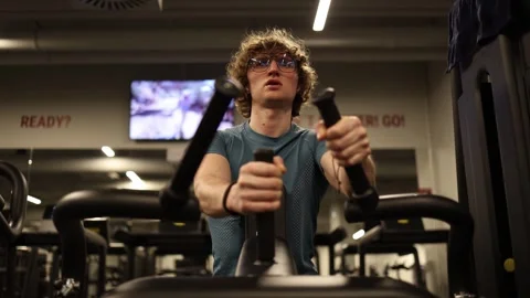 A person is using an elliptical machine in a modern gym, focusing on cardio exer Stock Footage 301677132