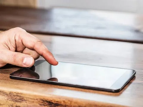 Person using finger on tablet screen on wooden table Stock Photos