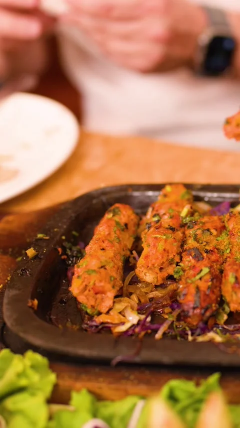 Person Using Fork to Pick Up Grilled Seekh Kebab from Sizzler Plate Stock Footage 337535110