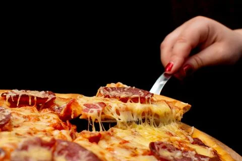 A person is using a fork to pick up a slice of pizza from the table Stock Photos