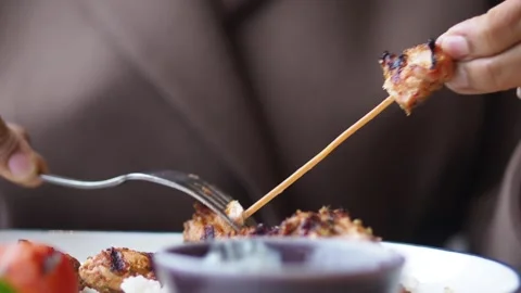 Person using fork to remove grilled chicken pieces from wooden skewer over .. Vidéo 331836046
