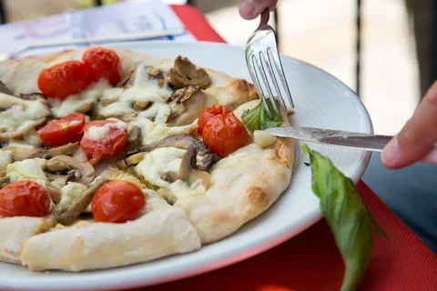 A person is using a fork to slice a pizza into pieces. Round pizza marinara with Stock Photos