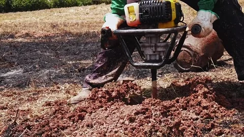 Person using a gas powered earth auger to drill a hole in the soil Stock Footage 344040060