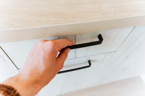 A person is using a gesture to open a drawer with a black hardwood handle Foto stock