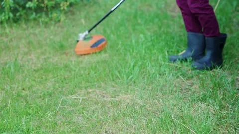 A Person Using a Grass Trimmer to Tidy Up a Lush Green Lawn Surrounded by Stock Footage 312074600