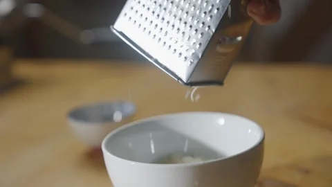A person is using a grater to grate cheese into a bowl Video stock 306042764