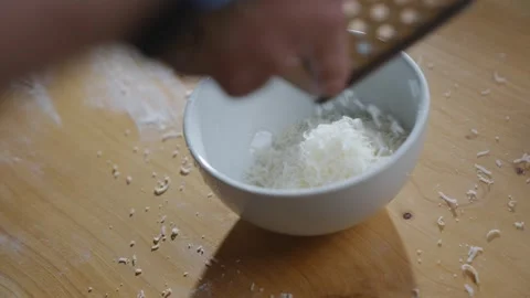 A person is using a grater to grate some cheese into a bowl Stock Footage 306042784