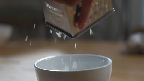 A person is using a grater to sprinkle sugar on a bowl Stock Footage 306042776