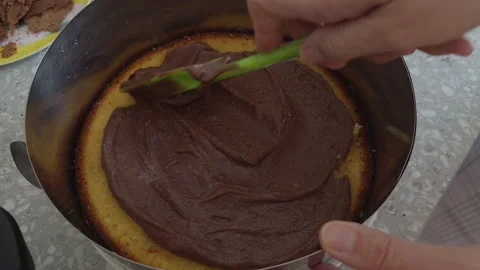 A person using a green spatula to spread thick chocolate cream over sponge cake Stock Footage 330398551