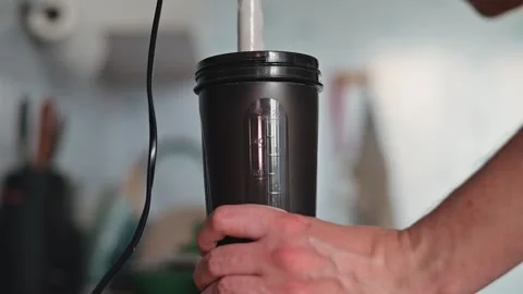 A person is using a hand-held blender to mix ingredients in a black container in Stock Footage 339096185