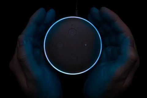 Person using an illuminated Amazon Echo Dot smart speaker. Stock Photos