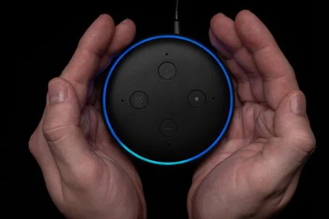Person using an illuminated Amazon Echo Dot smart speaker. Stock Photos
