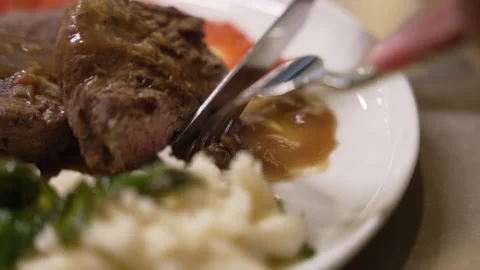 A person using a knife and fork to cut a piece of beef steak Stock Footage 338391376
