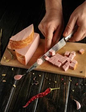 A person is using a knife to cut meat into small cubes on a wooden board. Spi Stock Photos