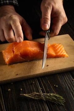 A person is using a knife to cut a piece of fresh salmon on a wooden cutting  Stock Photos