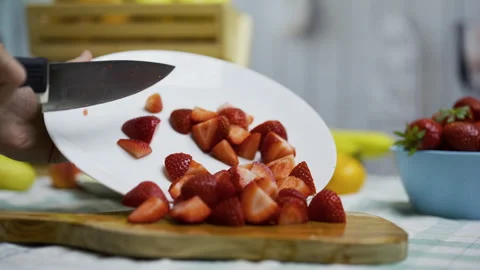 Person using knife to move sliced strawberries onto cutting board in kitchen, Stock Footage 341187746