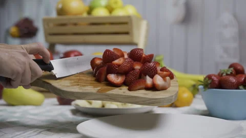 Person using knife to scrape cut strawberries onto white plate in kitchen - Stock Footage 341026795